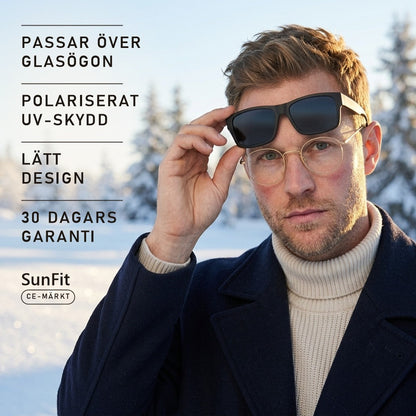 Man med glasögon lyfter SunFit fit-over-solglasögon i vintersol över snö
